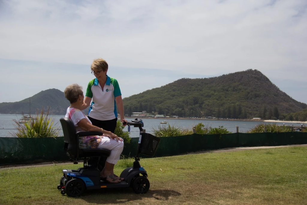 A Care For You at Home staff member standing beside a senior woman using a wheelchair