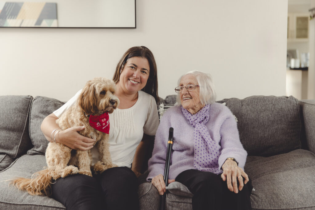 A woman holding a dog is seated on the couch beside a senior woman