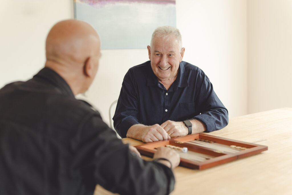 Two men seated at a table playing backgammon.