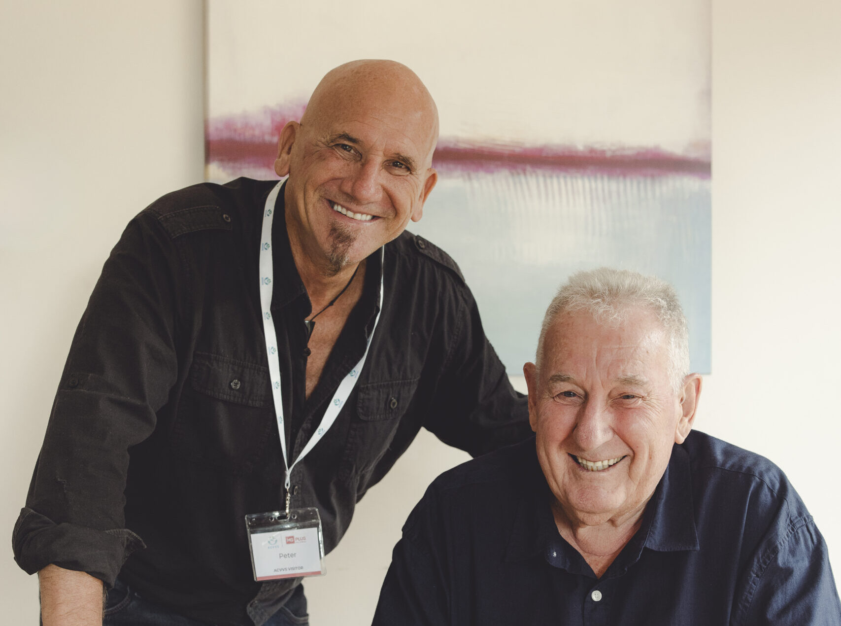 A man standing beside a senior man who is seated at a table