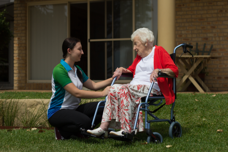 A Care For You at Home staff member kneeling beside a senior woman seated in a wheelchair