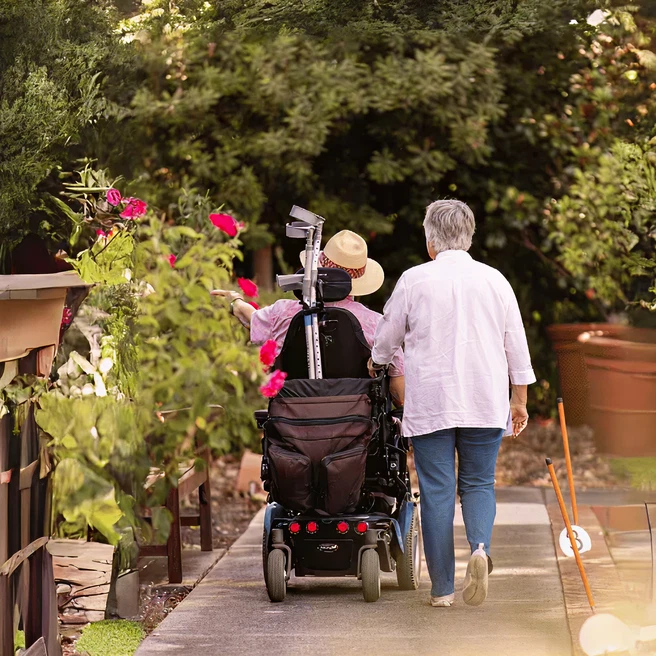 Veterans home care - A senior woman walking beside a senior man who is using a wheelchair