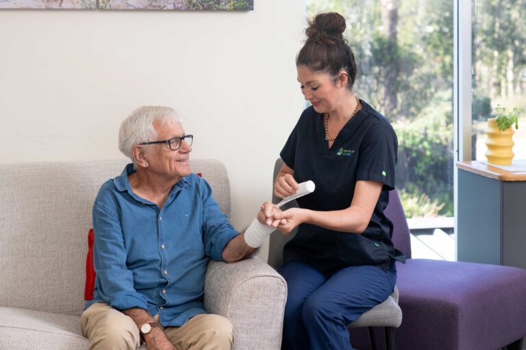 A senior man having his arm bandaged by a Care for You at Home staff member